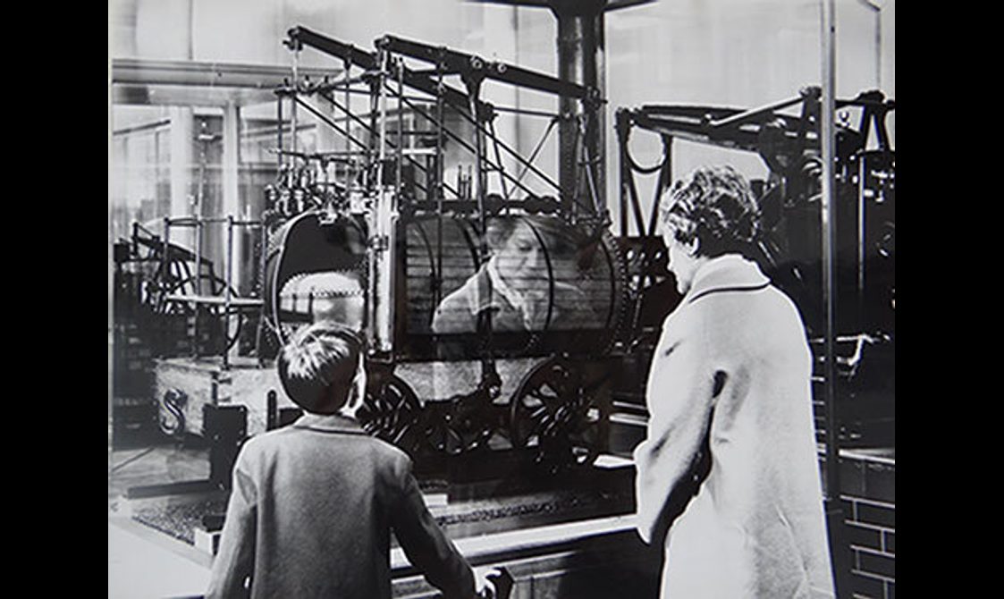 A black and white image of a woman and a child looking at a train model in a museum.
