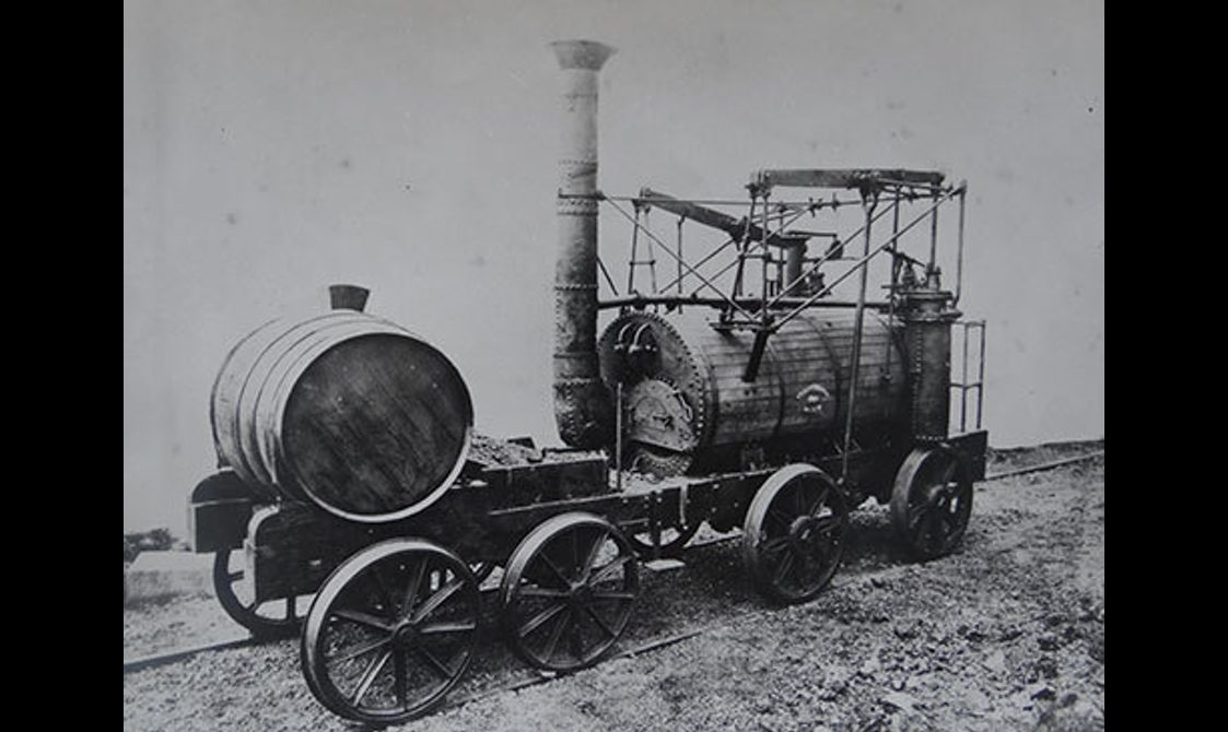 A black and white image of a train steam engine.