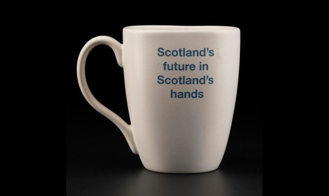 Simple white mug, tall but not overly so, with an earlobe-shaped handle and text in indigo blue reading 'Scotland's future in Scotland's hands'.