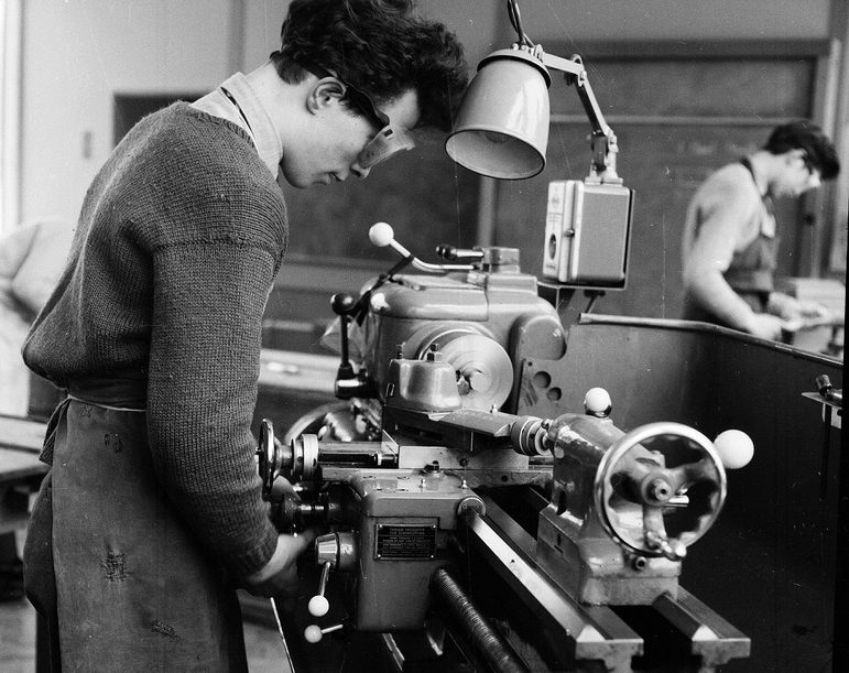 A black and white photograph of a person wearing goggles and using machinery