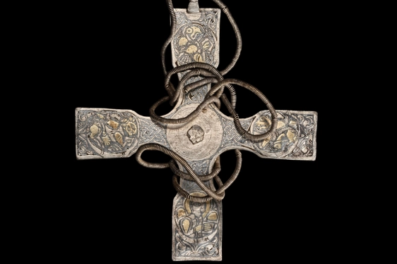 A tarnished cross pendant with celtic details on its surface. A chain is wrapped around the cross.