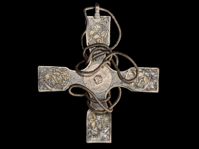 A tarnished cross pendant with celtic details on its surface. A chain is wrapped around the cross.