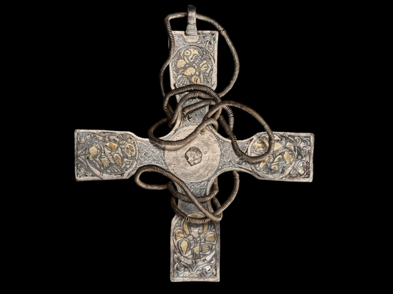 A tarnished cross pendant with celtic details on its surface. A chain is wrapped around the cross.