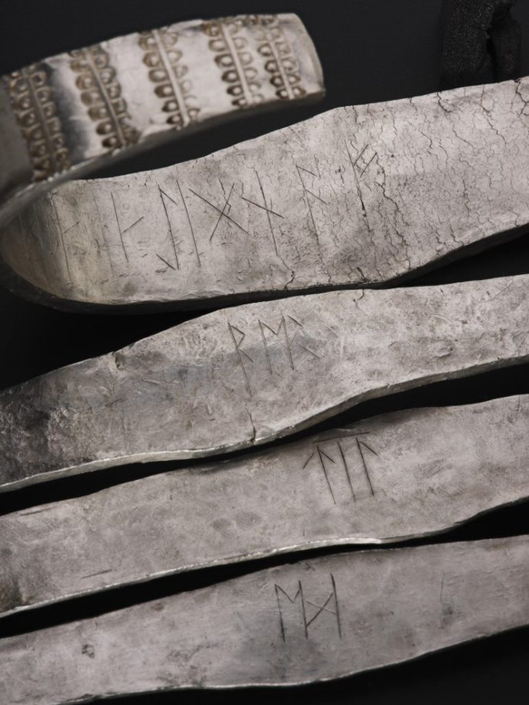 4 thin silver arm-bands, with runic inscriptions on the inside. The bottom 3 arm bands are flattened, but the top one has a curve at one end.