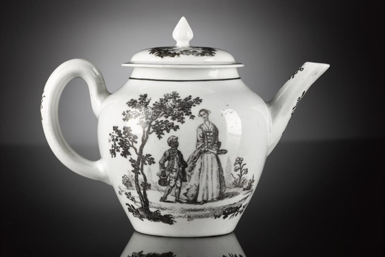 A white teapot with illustrations in black of a woman in a dress with a fitted corset and full skirt beside a young man in a long jacket carrying a teapot. There are trees and flowers surrounding them.