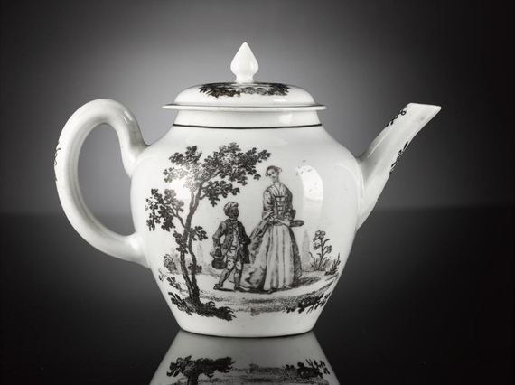 A white teapot with illustrations in black of a woman in a dress with a fitted corset and full skirt beside a young man in a long jacket carrying a teapot. There are trees and flowers surrounding them.