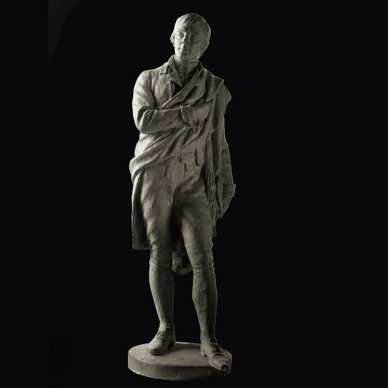 A grey statue of Robert Burns, a young man in trousers, long socks, and a jacket with a sash across his body.