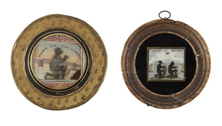Two round plaques with wooden frames and pictures showing enslaved people kneeling in metal metal shackles and chains with slave ships at sail in the distance.